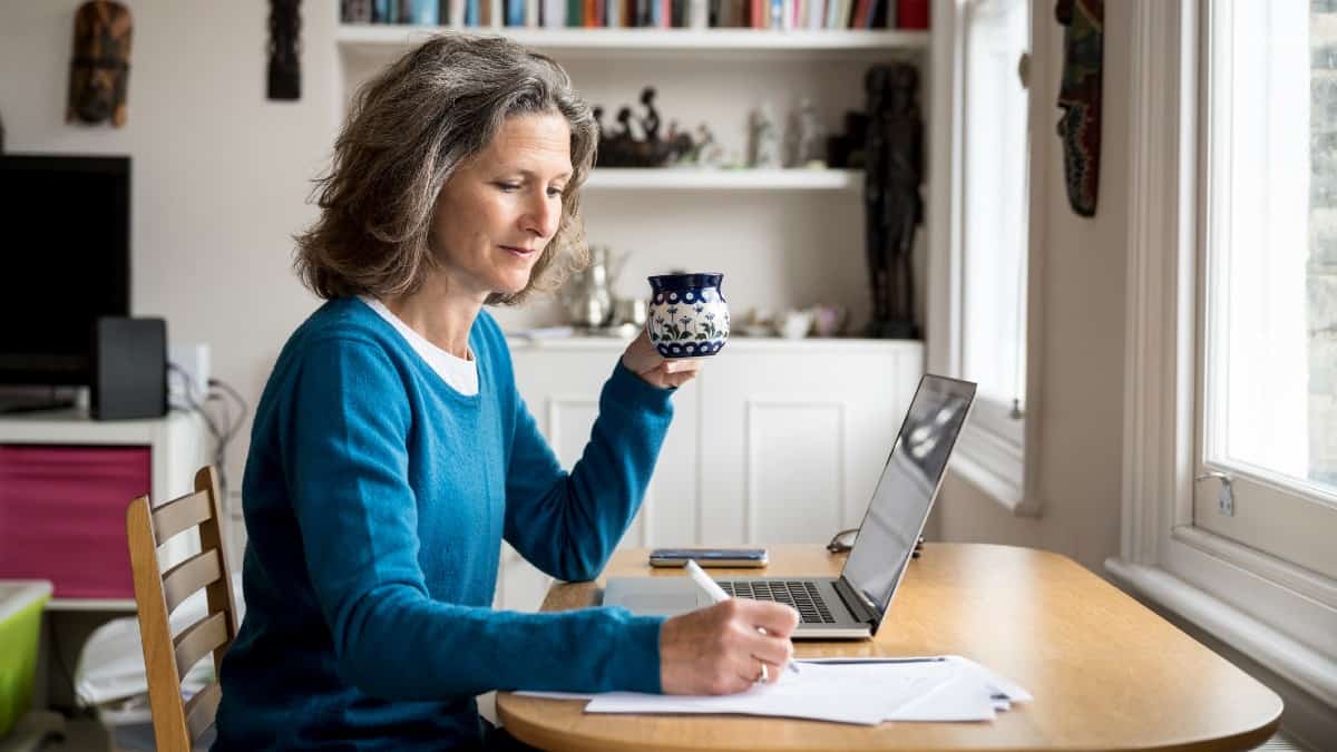 Ώριμη καυκάσια γυναίκα που κάθεται σε ένα τραπέζι με καφέ και φορητό υπολογιστή κρατώντας σημειώσεις σε χαρτί