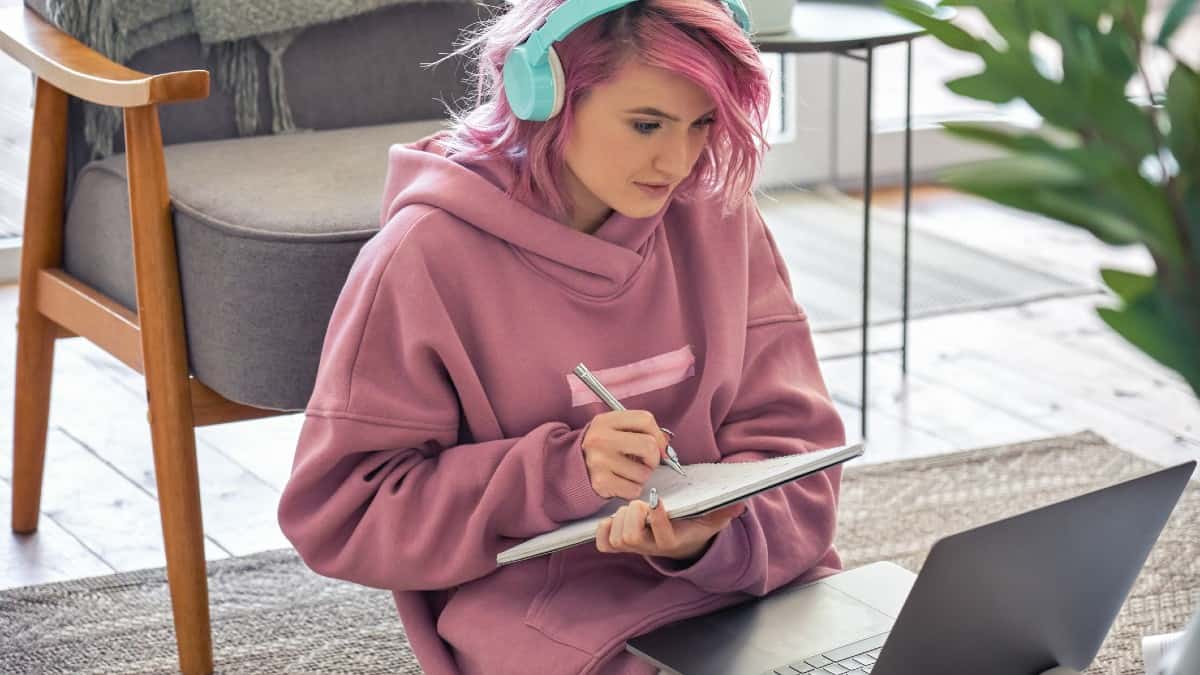 Νεαρή καυκάσια γυναίκα με ροζ που μελετά από την οθόνη του φορητού υπολογιστή της