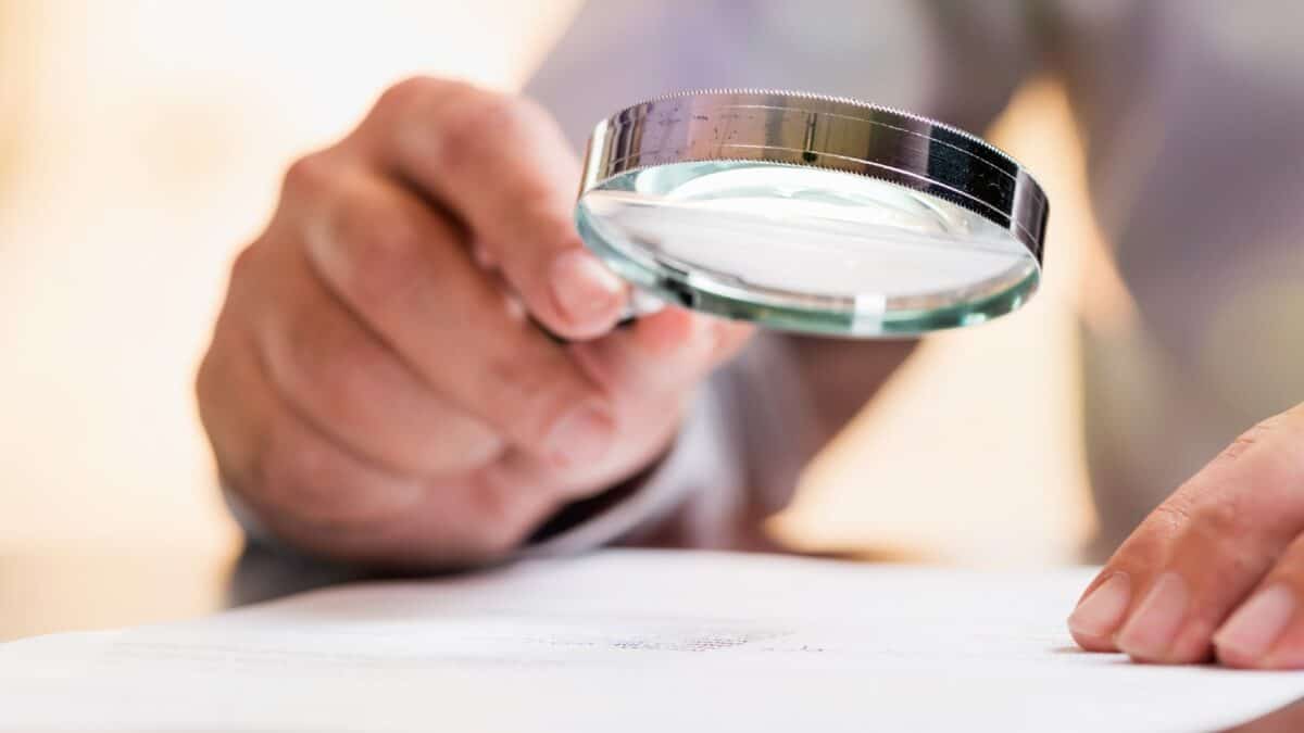 Person holding magnifying glass over important document, reading the small print