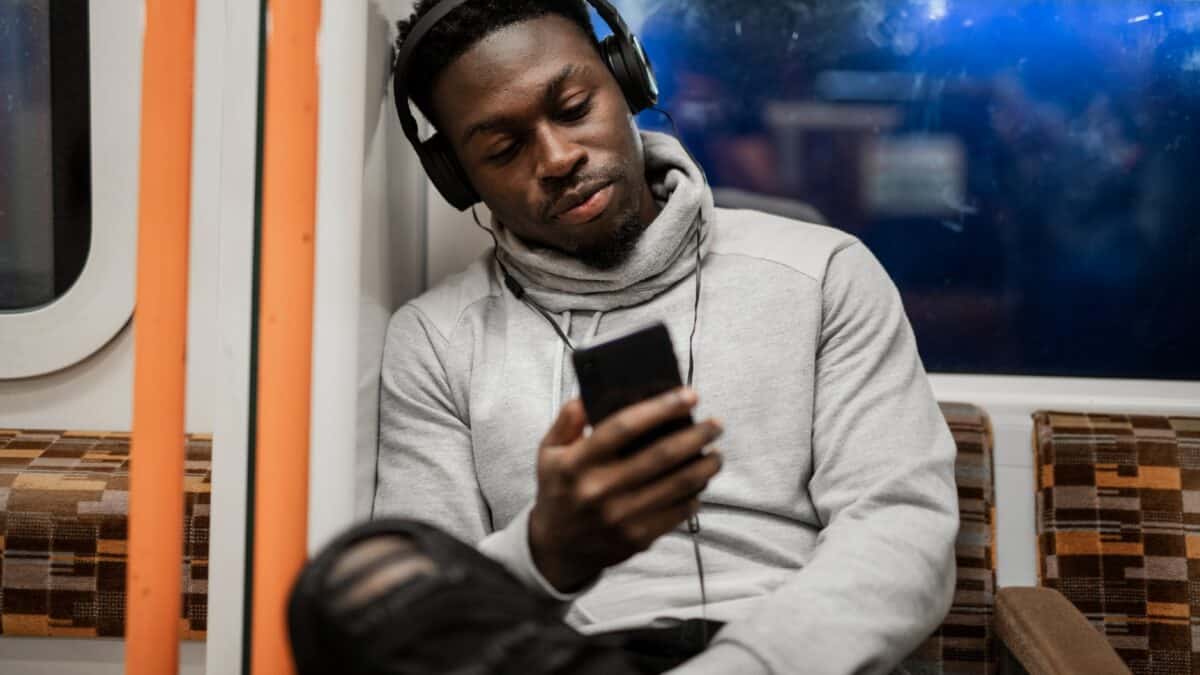 लंदन ओवरग्राउंड पर युवा अश्वेत व्यक्ति फ़ोन देख रहा है